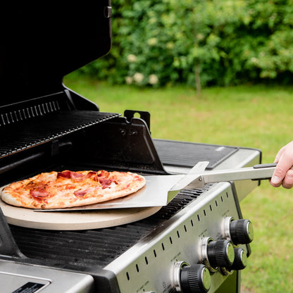 Person placing a pizza on a grill outdoors