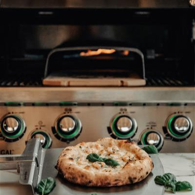 Pizza being taken out of a Broil King grill on a marble surface